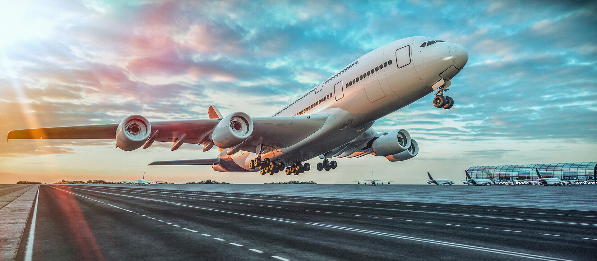 Large commercial airplane taking off from a runway at sunset with a vibrant sky and airport terminal in the background.